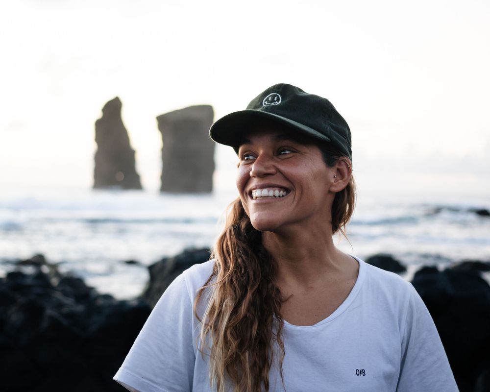 Isabela Sousa sorrindo em frente ao mar, com o litoral ao fundo.