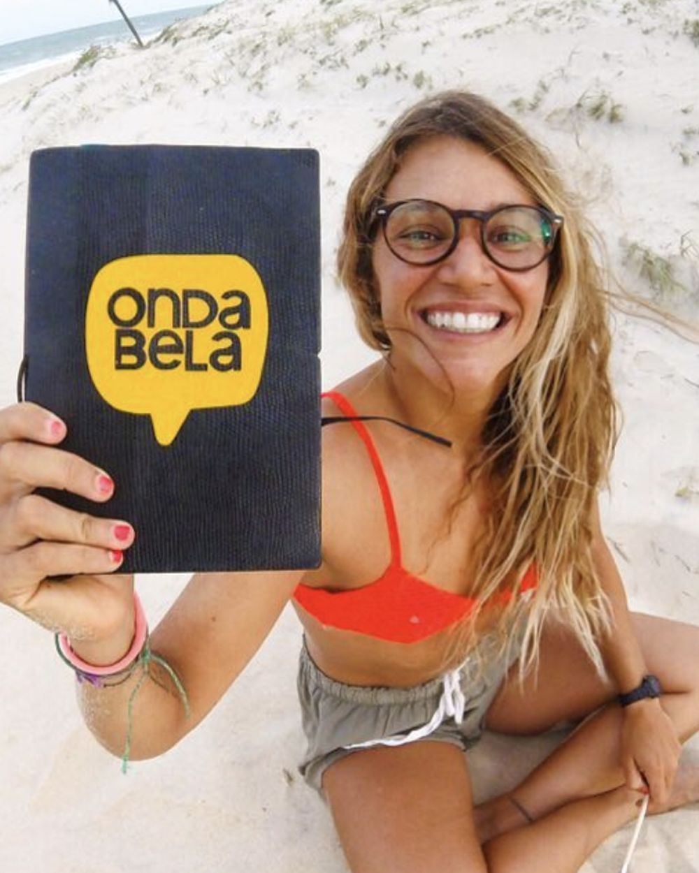 Isabela Sousa na praia segurando um caderno com a marca Onda Bela.